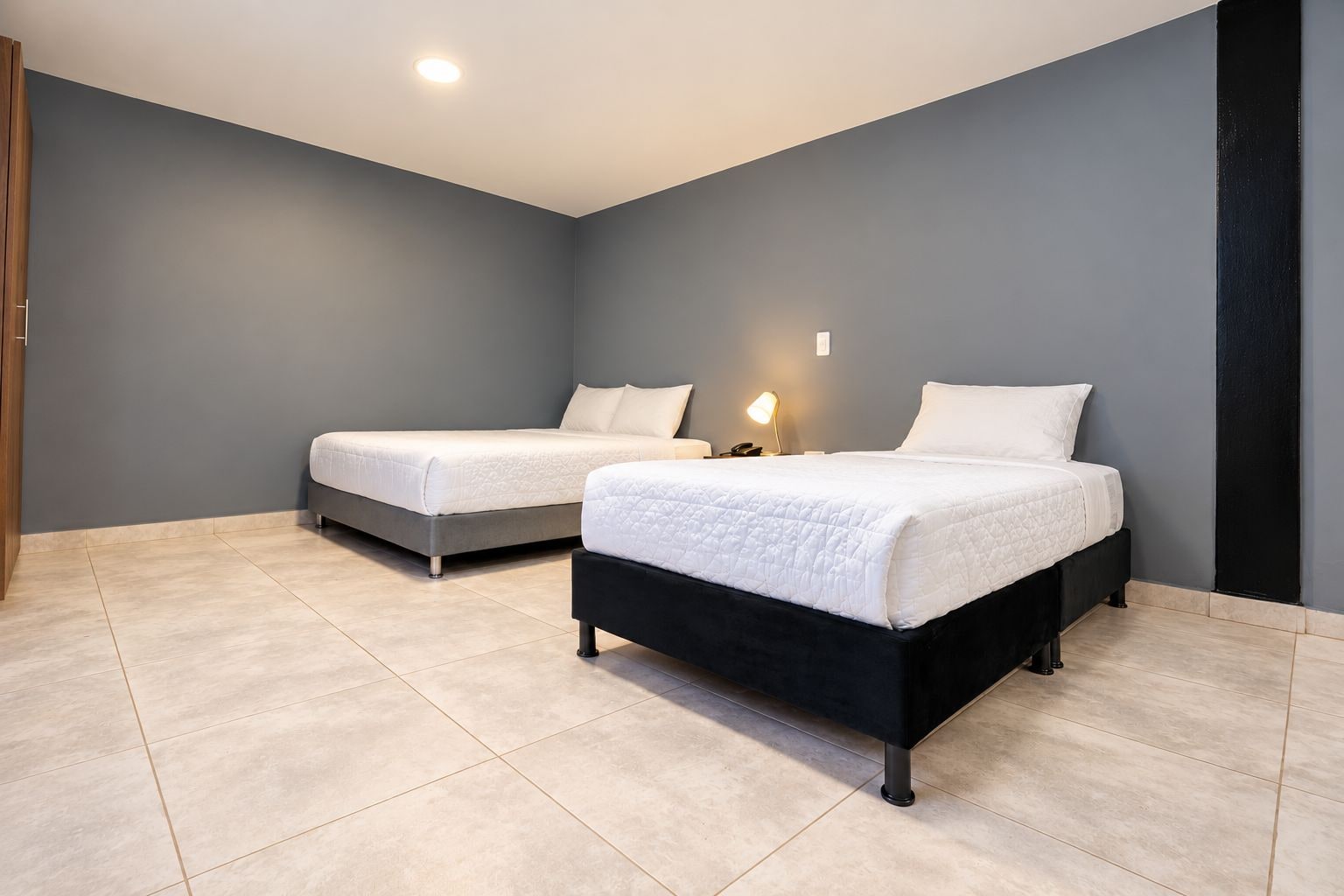A room with two beds, a nightstand, a lamp, and a wooden door.