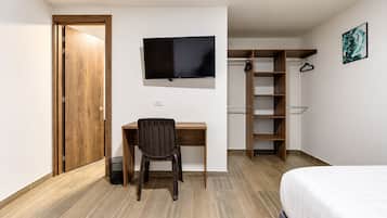 Un dormitorio con cama, escritorio con silla, televisor, armario y un cesto de basura.