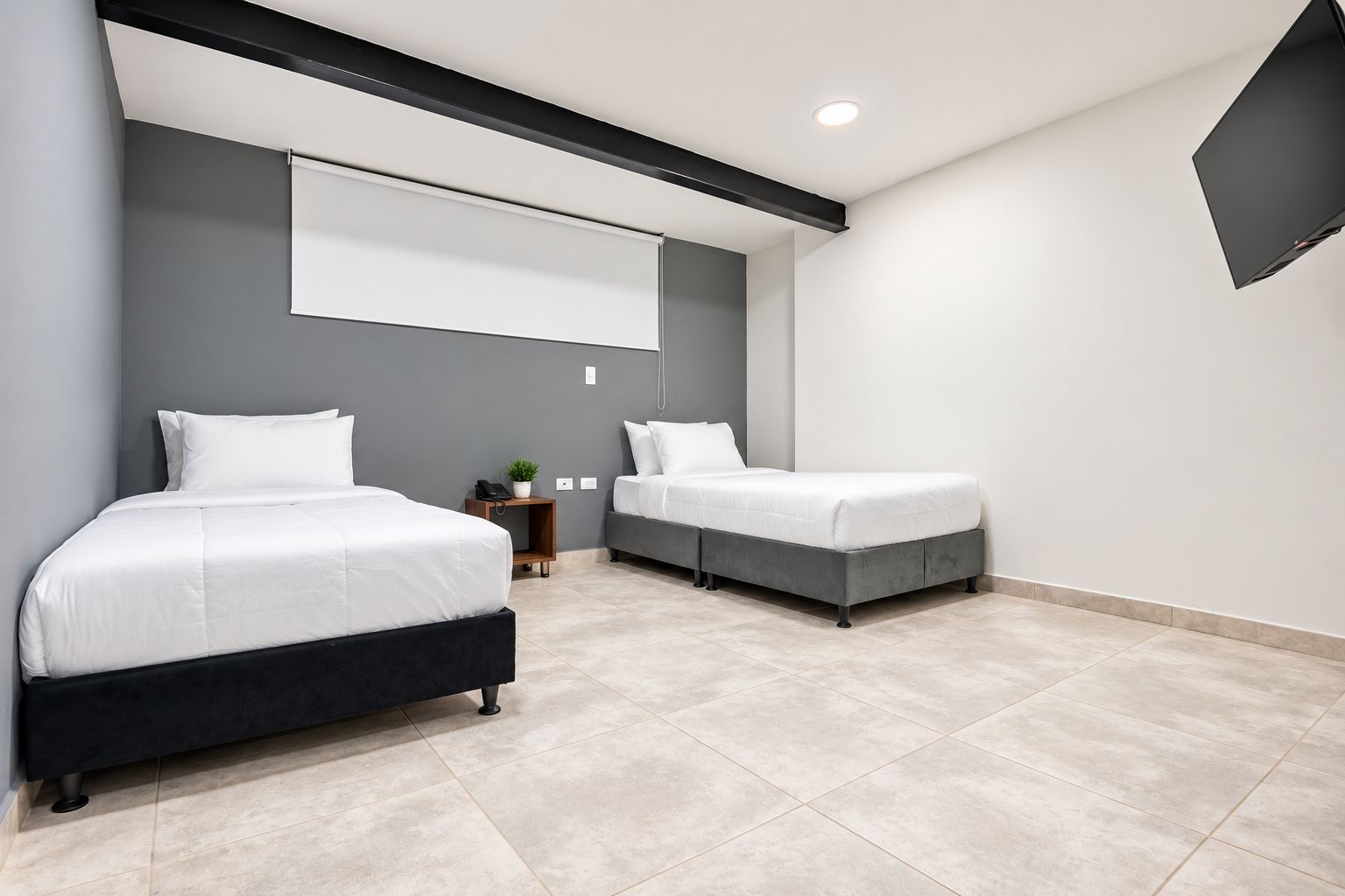 A modern bedroom with two beds, a small bedside table with a lamp, and a large window.