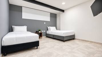 A modern bedroom with two beds, a small bedside table with a lamp, and a large window.