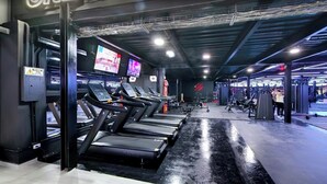 Un gimnasio con cintas de correr, máquinas de pesas y una pantalla grande que muestra un evento.