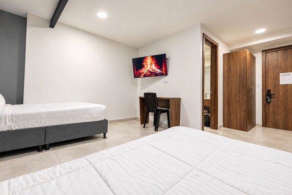 A hotel room with two beds, a desk, a TV, and wooden wardrobes. - XLiving Host & Rooms (Bogotá)