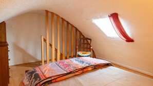 A bedroom with a sloped ceiling, a wooden chair, a bed with a colorful blanket, and a window with red curtains. - 2-person rental in Les Badieux (BONDONS (LES))