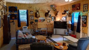 Interior acogedor de una cabaña con techo de madera, venados montados como decoración, un televisor y un sofá con mantas.