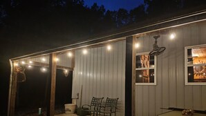 Un espacio al aire libre cubierto con luces colgantes, una mesa, sillas y un ventilador.