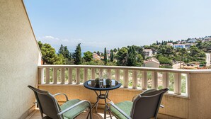 Ein Balkon mit rundem Tisch und zwei Stühlen, mit Blick auf eine Küstenstadt mit Häusern und Bäumen.