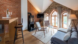 A cozy loft-style room with a brick wall, a fireplace, a TV, a sofa, and a dining area with stools. - HexenburgbeiDresden 2 Zimmer Architektenwohnung mit eigener Sauna, Whirlwanne und Kamin - Nähe Sächsische Schweiz (Grossharthau)