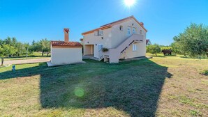 A two-story house with a red-tiled roof, a small attached structure with a chimney, and a well-maintained lawn. - Emila's Apartment- Blue (Nin)