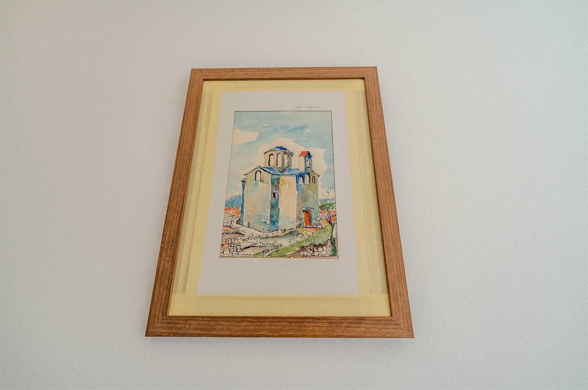 A framed watercolor painting of a building with a dome and two towers, possibly a church or historical structure, on a plain wall.