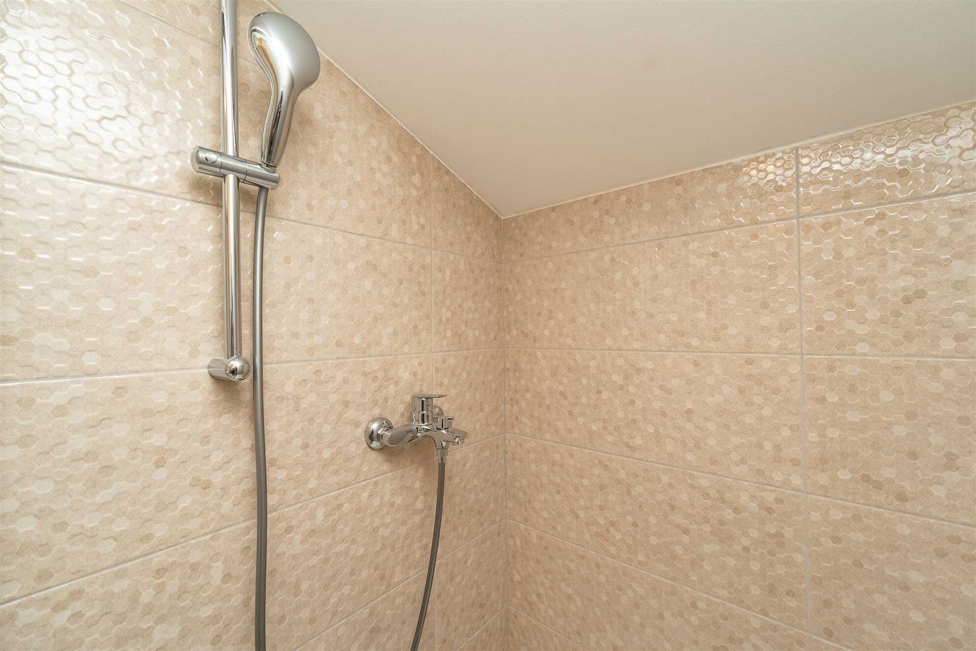 A shower with a handheld showerhead and a wall-mounted faucet in a tiled room.