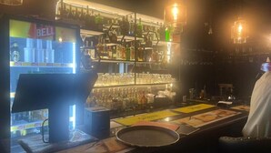 A bar area with a refrigerated display, shelves of bottles, and a counter with a menu. - ROYAL COMPLEX HOTEL AND APARTMENTS (Kampala)
