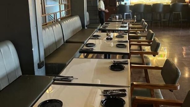 A restaurant with long communal tables, individual booths, and a bar area. - ROYAL COMPLEX HOTEL AND APARTMENTS (Kampala)