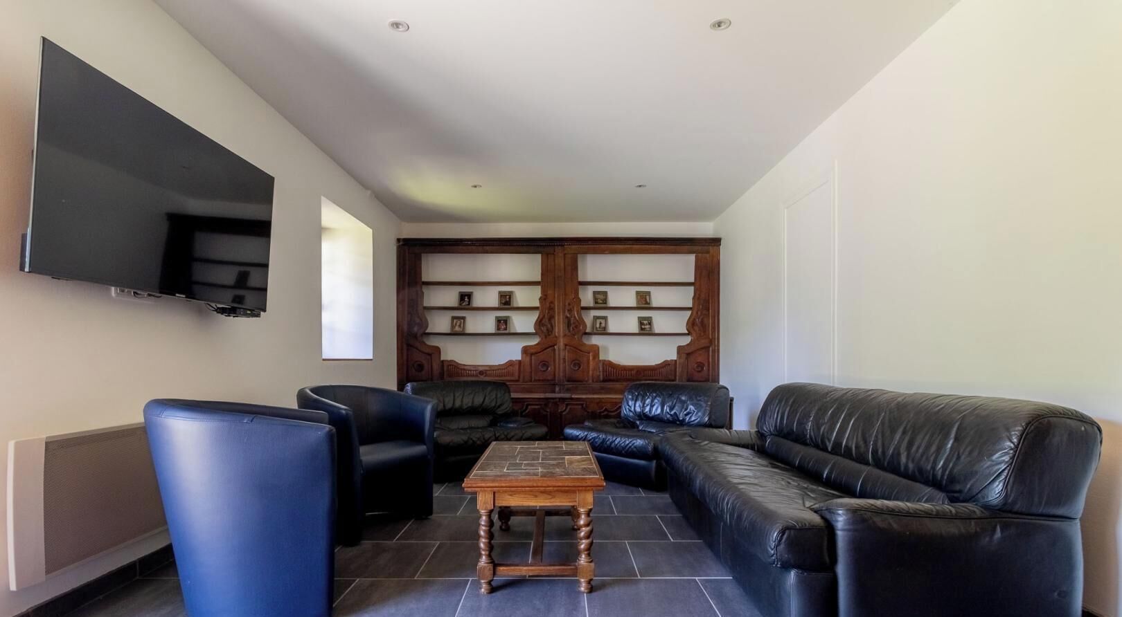 A living room with a TV, leather sofas, a coffee table, and a wooden cabinet with shelves.