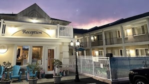 A hotel reception with a balcony, American flags, and a fenced parking area. - The Lamplight Inn (Lavallette)