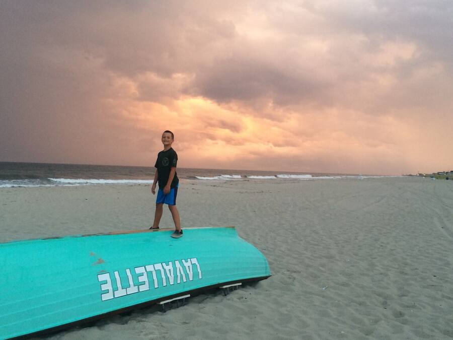 Une personne se tient debout sur une plateforme verte utilisée par les sauveteurs, sur laquelle on peut lire le mot « Sauveteur », sur une plage de sable, avec l’océan en arrière-plan.