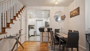 A modern kitchen with white cabinets, a dining area with a marble table, and a staircase with wooden steps.