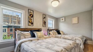 A bedroom with two beds, large windows, and artwork on the walls.