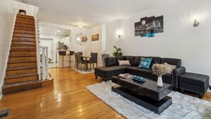 A modern living room with a staircase, a dining area, and a black leather sofa.