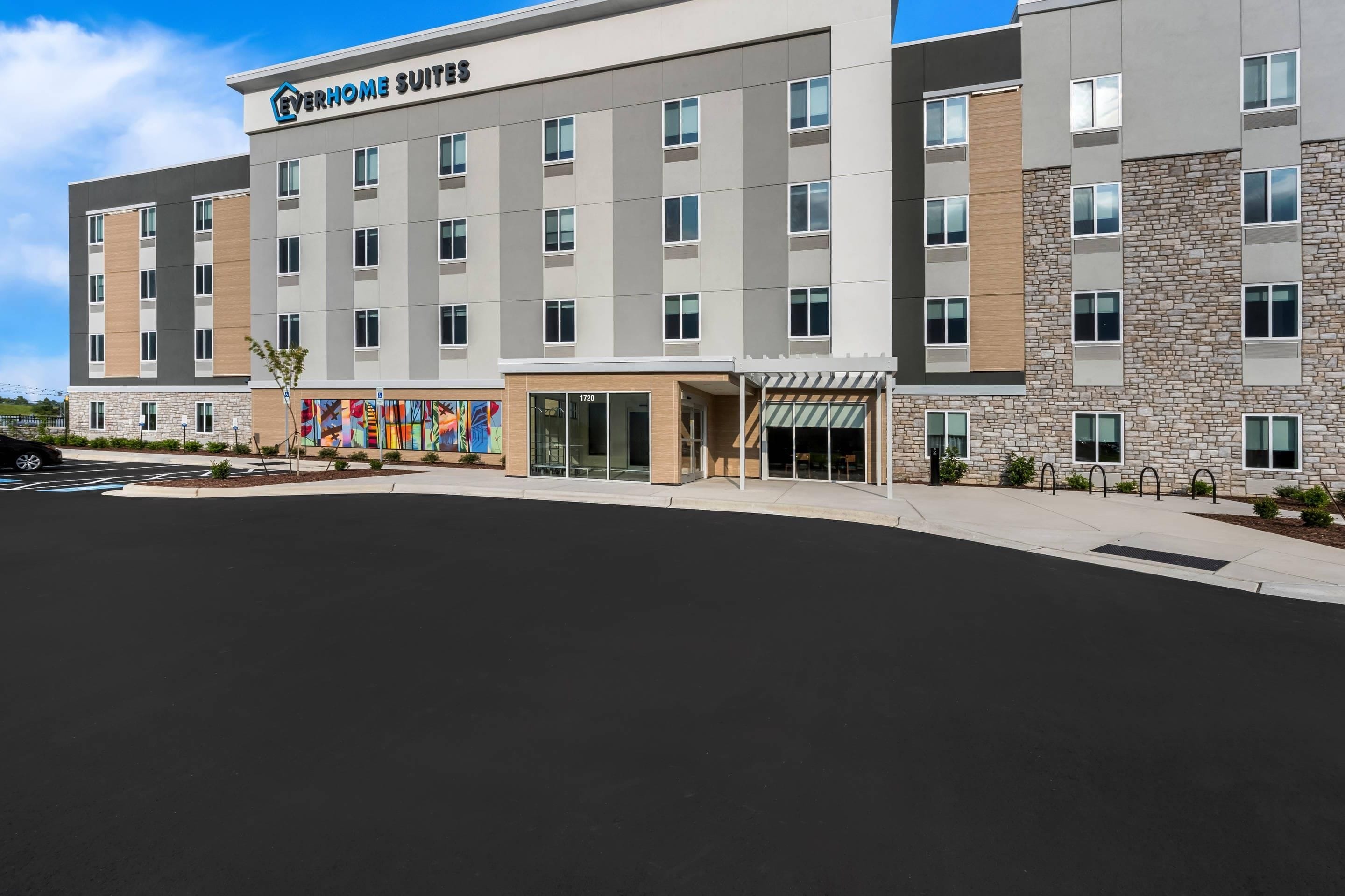 A modern hotel building with a flat roof, multiple windows, and a sign reading 'Everhome Suites'.