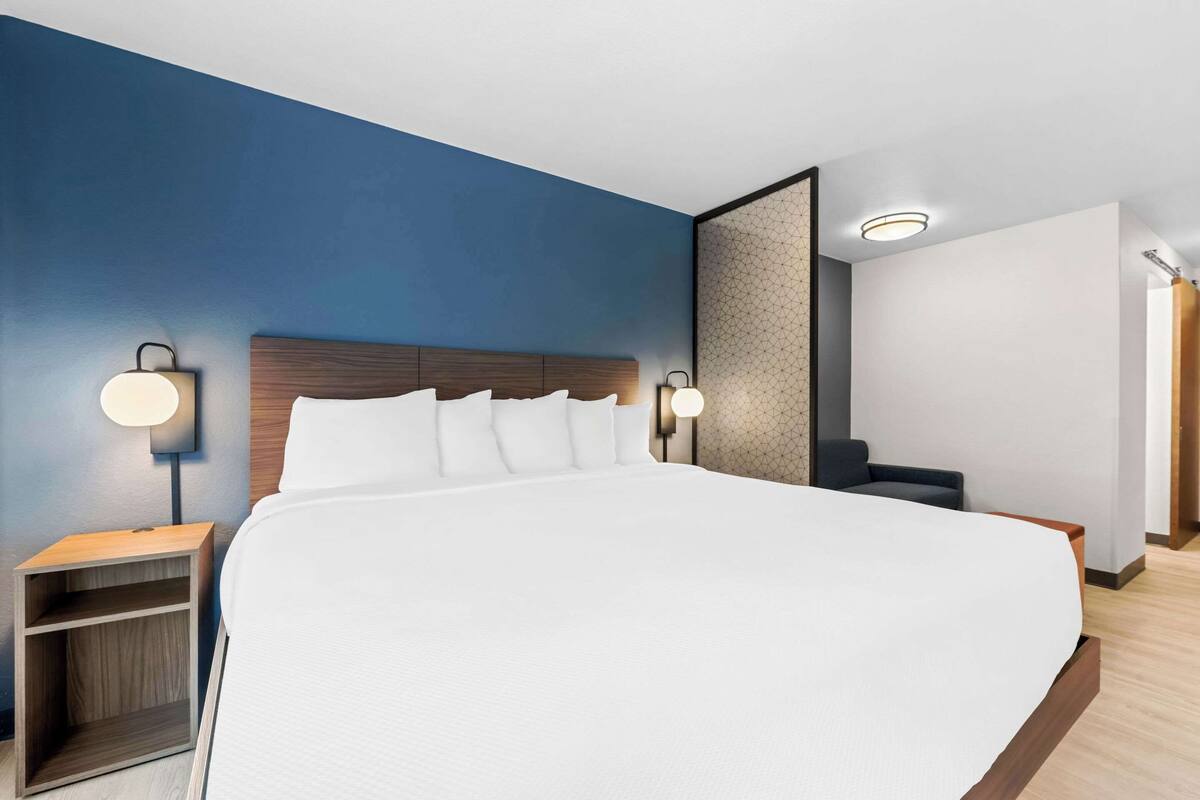 A modern hotel room with a large bed, two bedside tables, and wall-mounted lamps.