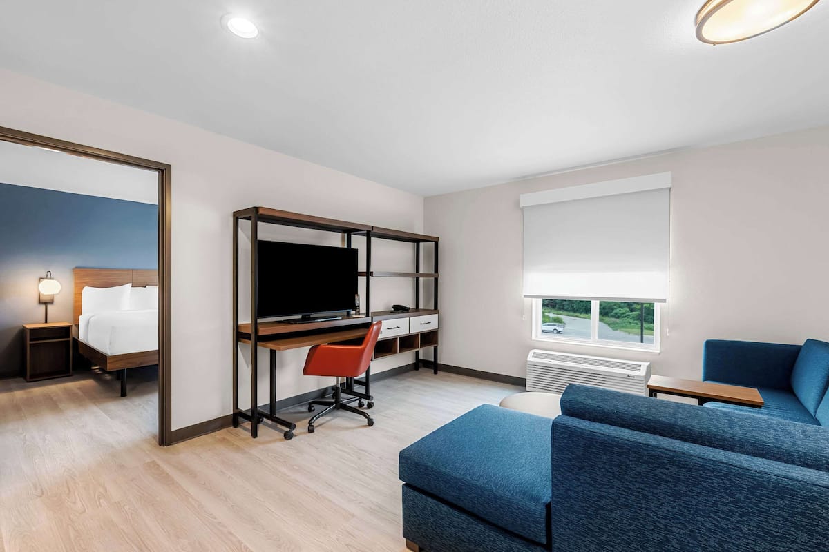 A modern hotel room with a bed, a desk with a computer, a blue sofa, and a large window.
