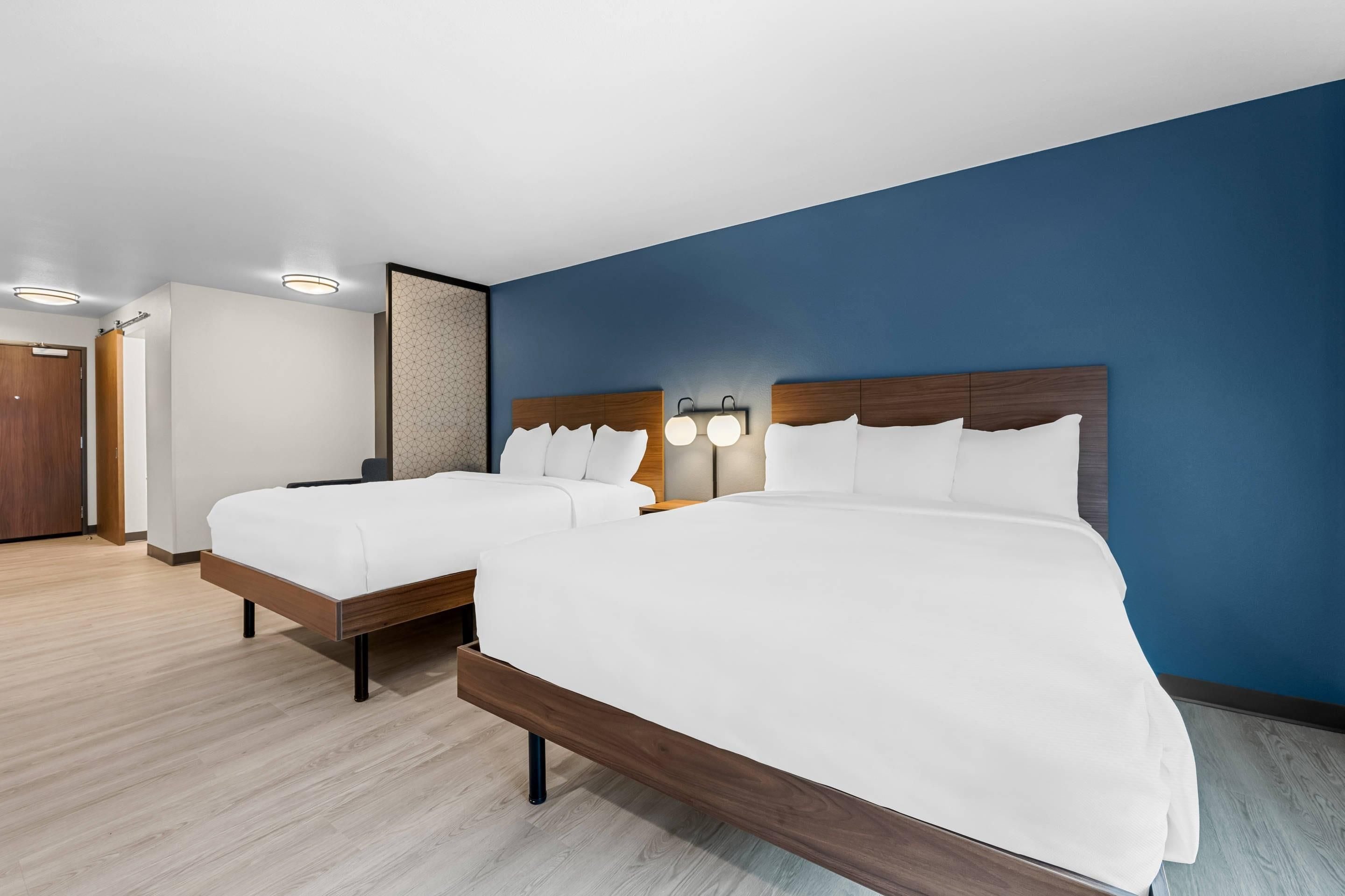 Una habitación de hotel con dos camas, piso de madera y una pared azul decorativa.