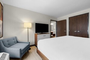 Habitación de hotel con cama, escritorio con televisor de pantalla plana, una silla, lámpara y armario.