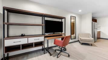 A modern room with a built-in TV, a desk with drawers, a red office chair, a sofa, and a refrigerator.