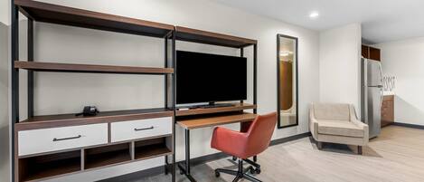 A modern room with a built-in TV, a desk with drawers, a red office chair, a sofa, and a refrigerator.