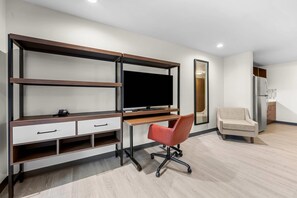 Una habitación moderna con televisor integrado, escritorio con cajones, silla de oficina roja, sofá y refrigerador.