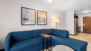 Un salon moderne avec un canapé d’angle bleu, une petite table d’appoint en bois et deux tableaux abstraits encadrés accrochés au mur.