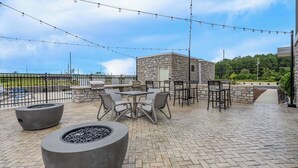 Un área de patio al aire libre con asientos de piedra, fogones y luces colgantes.