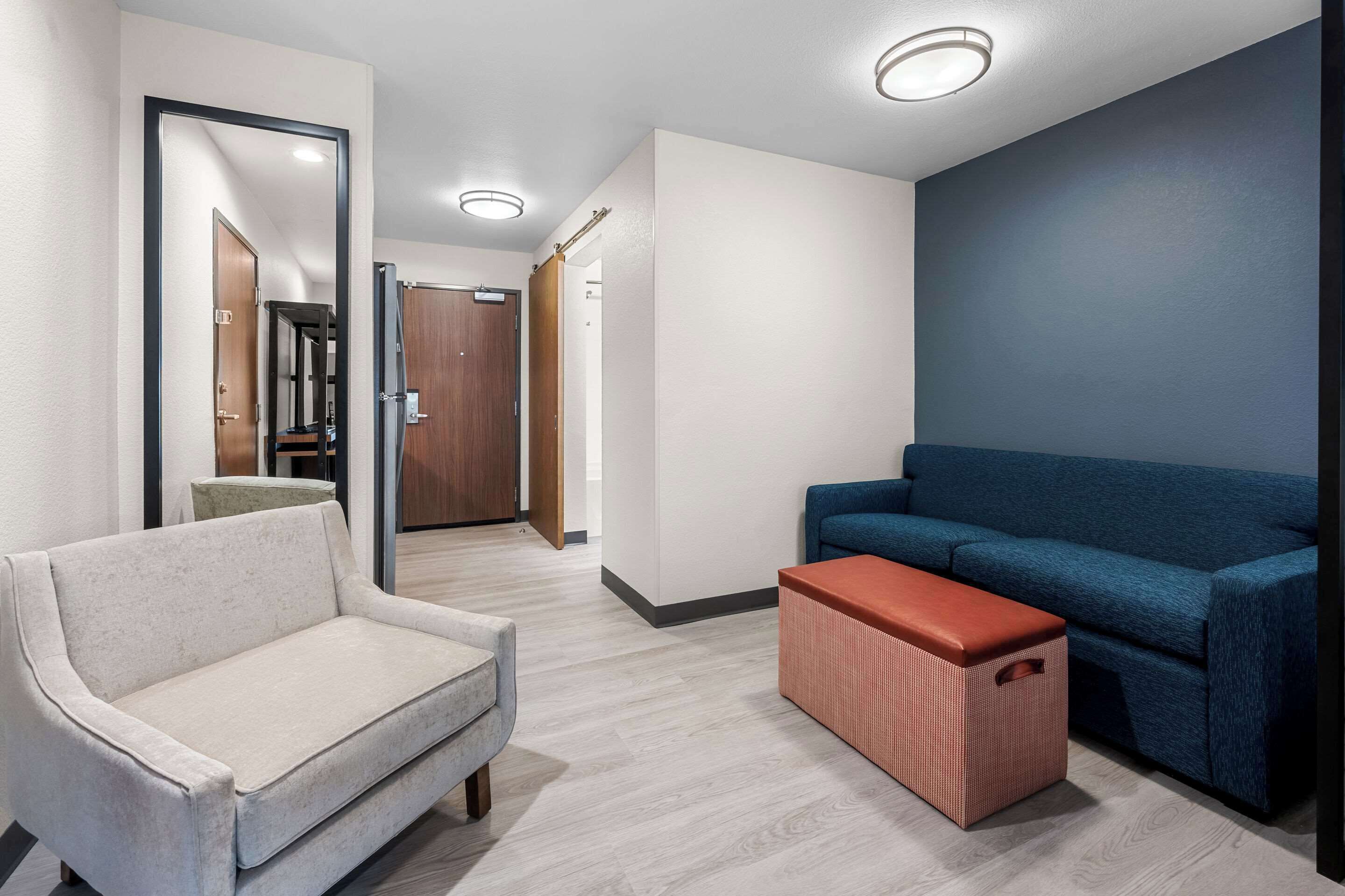 A modern hotel lobby with a light-colored sofa, a blue sofa, and a red ottoman.