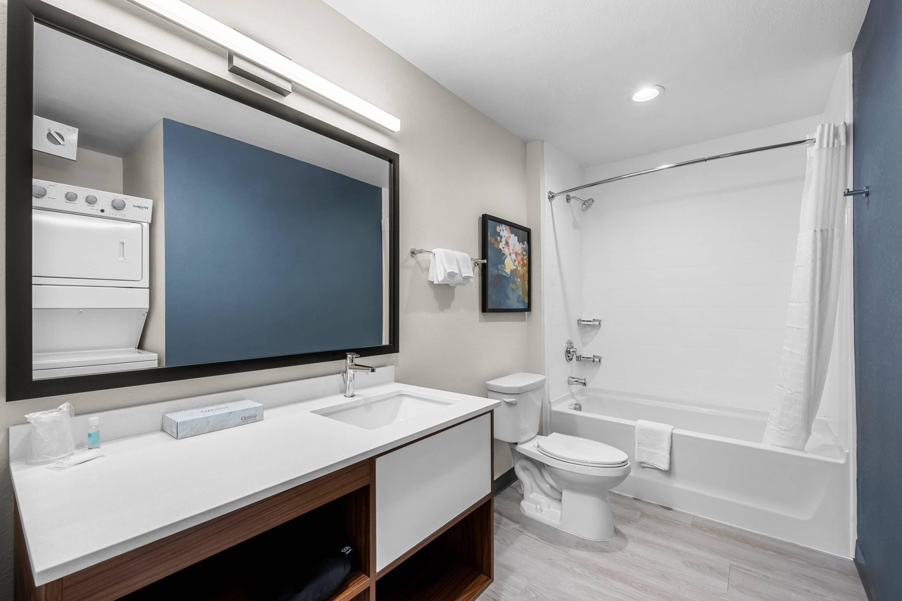 A modern bathroom with a large mirror, a white sink, a toilet, and a bathtub.