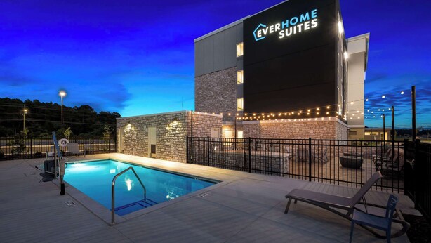 Exterior de un hotel con piscina, mobiliario de exterior e iluminación con luces colgantes.