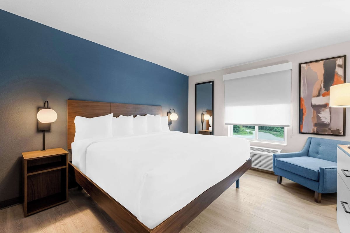 A modern hotel room with a large bed, bedside lamps, a desk, a chair, and a window with a view.
