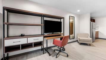 A modern room with a built-in TV, a desk with drawers, a red office chair, a sofa, and a refrigerator.