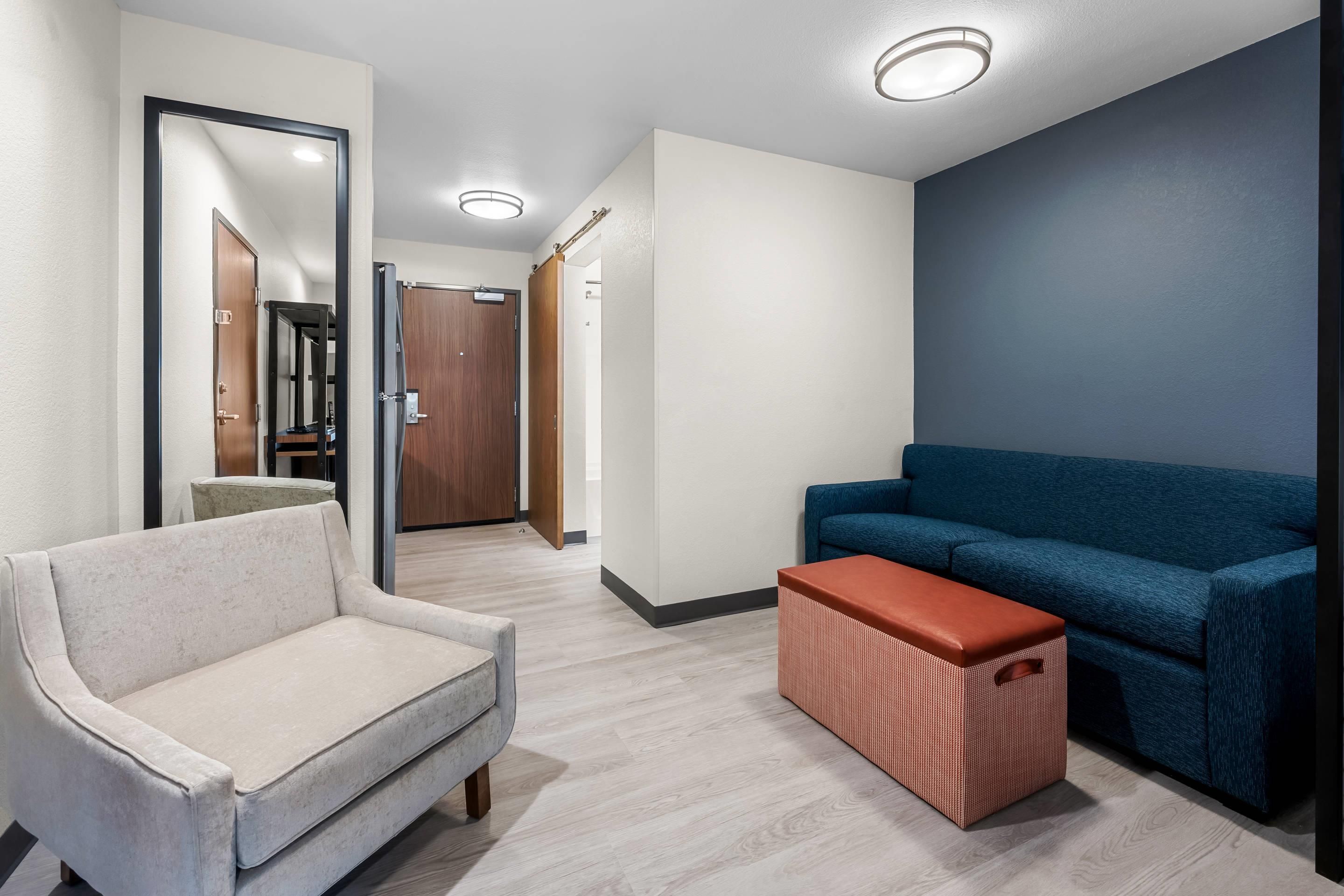 A modern interior with a light-colored armchair, a blue sofa, and a woven ottoman.