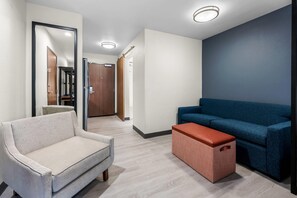 A modern interior with a light-colored armchair, a blue sofa, and a woven ottoman. - Everhome Suites Fayetteville near Fort Bragg (Fayetteville)