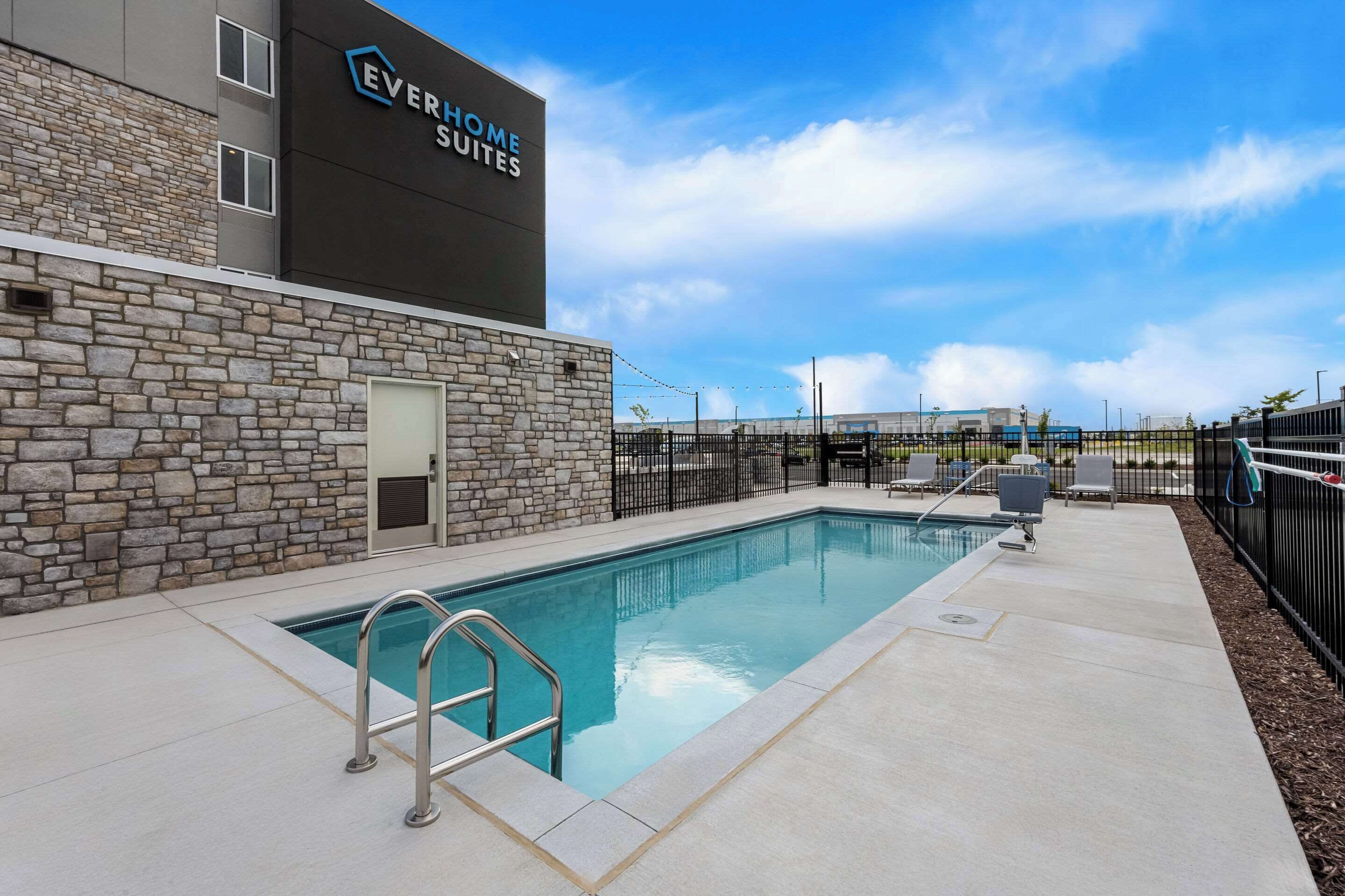 A swimming pool area with a stone wall, a pool ladder, and lounge chairs.