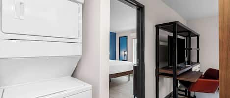 A modern hotel room with a built-in washer and dryer, a desk with a computer, and a red chair.