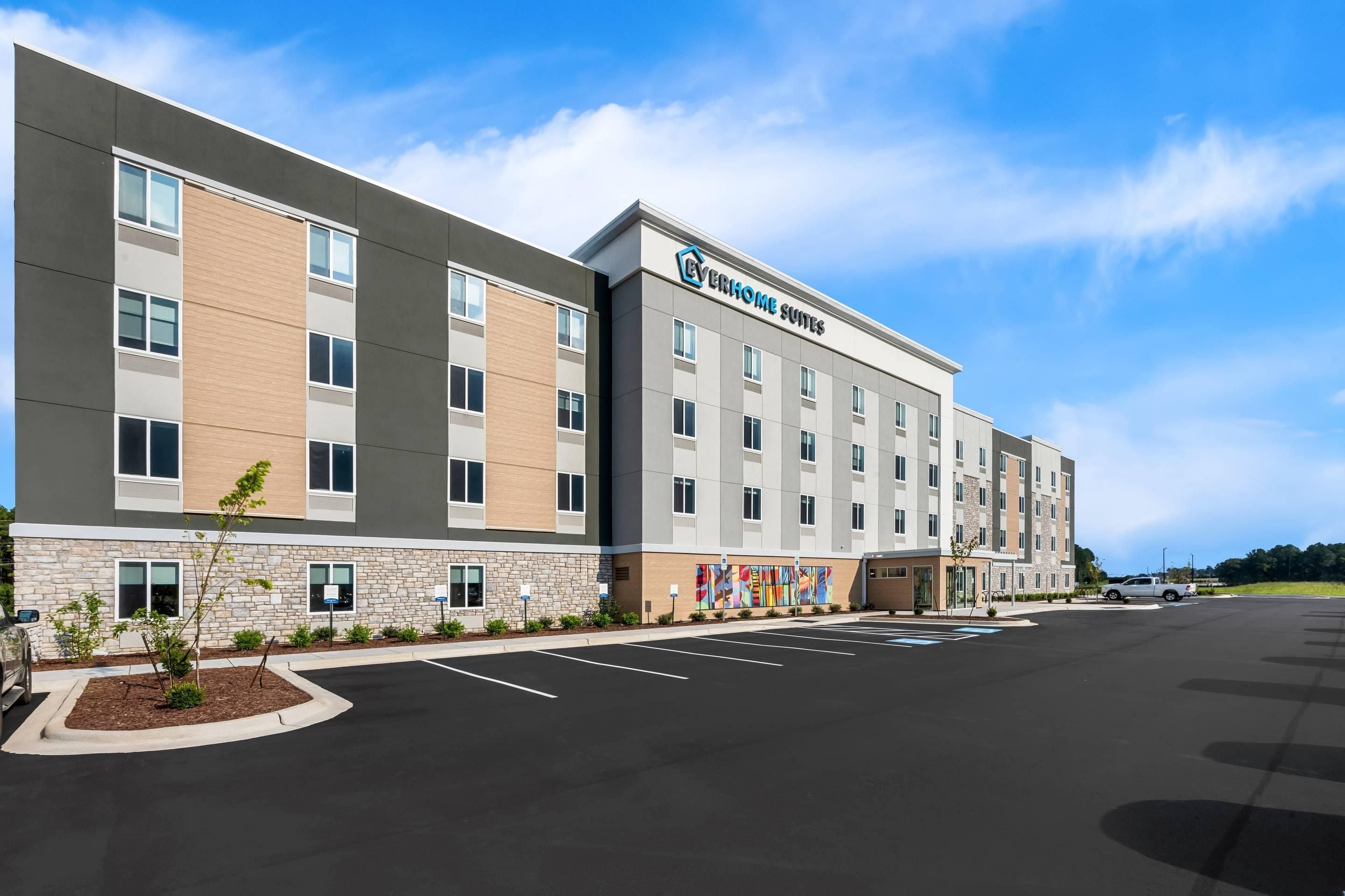 A modern hotel building with a flat facade, multiple windows, and a parking lot in front.