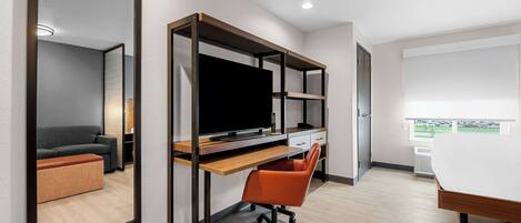 Un dormitorio moderno con una cama, un escritorio con computadora, una silla y un espejo grande.