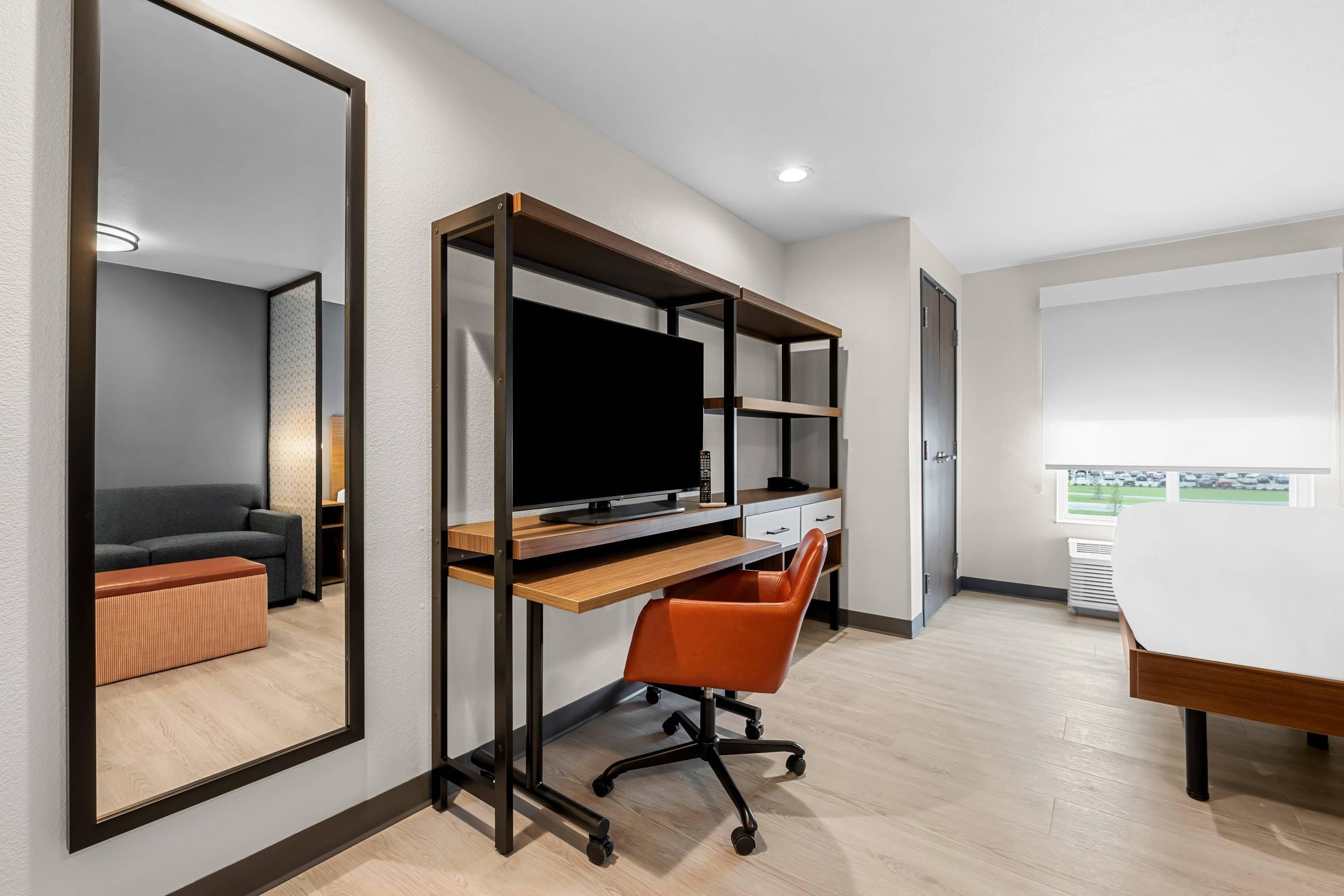 Una habitación de hotel moderna con un espejo grande, un escritorio con computadora, una silla y un sofá.
