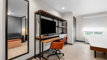 Una habitación de hotel moderna con un espejo grande, un escritorio con computadora, una silla y un sofá.