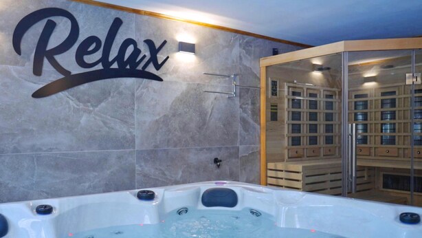 A spa area with a large tub, a wall with 'Relax' written on it, and a glass-enclosed sauna. - Nice home in Ogulin with sauna (Ogulin)