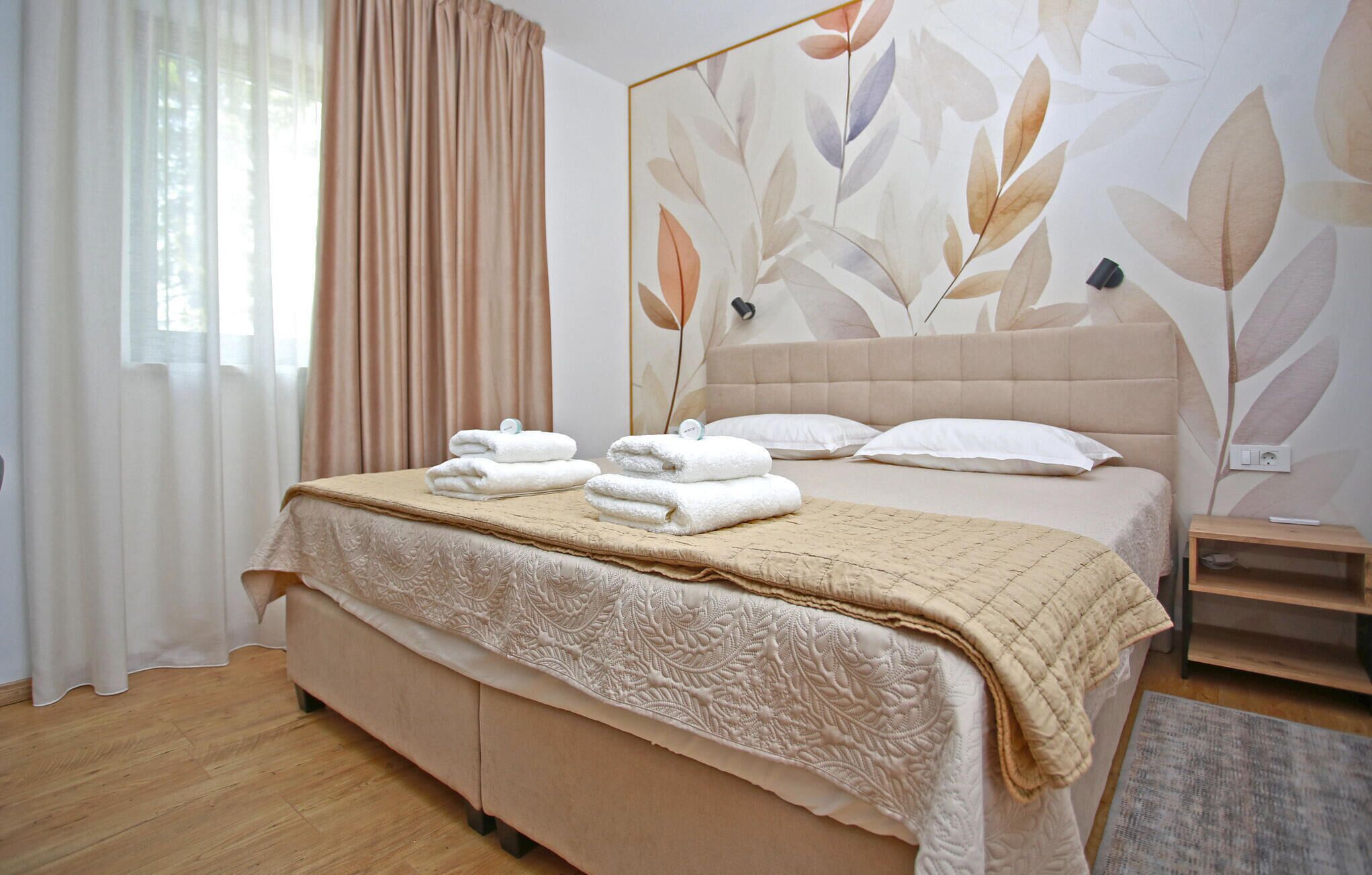 Una cama bien hecha con un cabecero color beige y un mural floral en la pared.