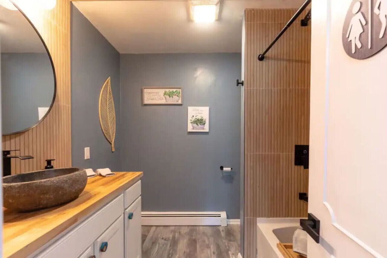 Un baño moderno con un espejo grande, tocador de madera y zona de ducha.