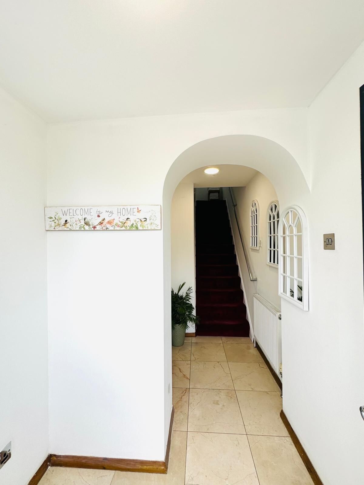 Un couloir avec une pancarte indiquant « BIENVENUE chez moi », un escalier et une plante en pot.