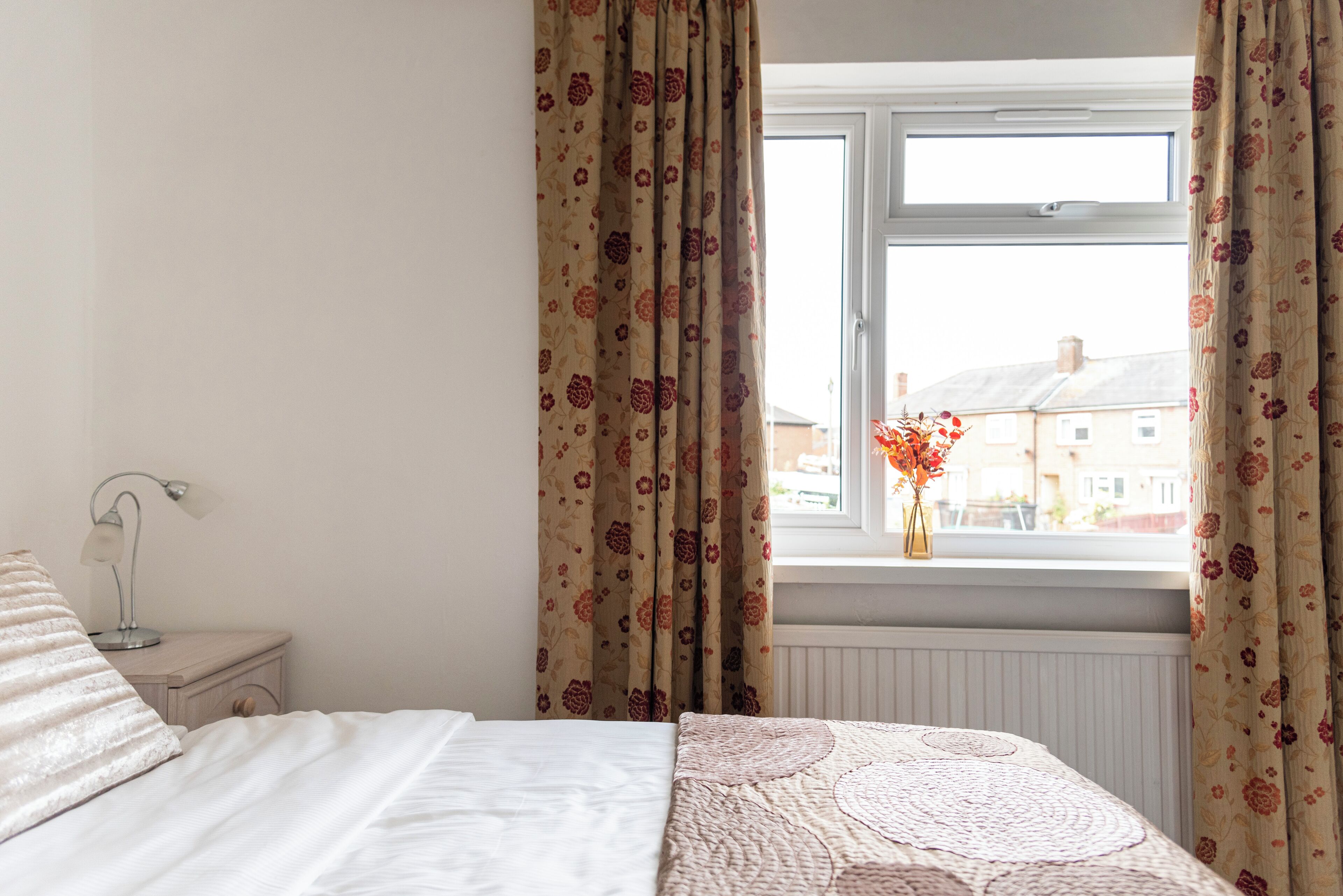Une chambre à coucher avec un lit, une table de chevet, une lampe et une fenêtre avec des rideaux.
